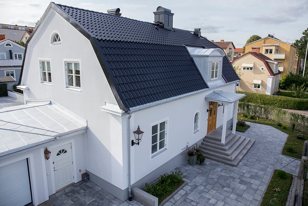 Vitt tvåvåningshus med svart tegeltak, vidbyggt garage, entré med trappa och asfalterad uppfart i ett förortskvarter. Takreparationer Jönköping