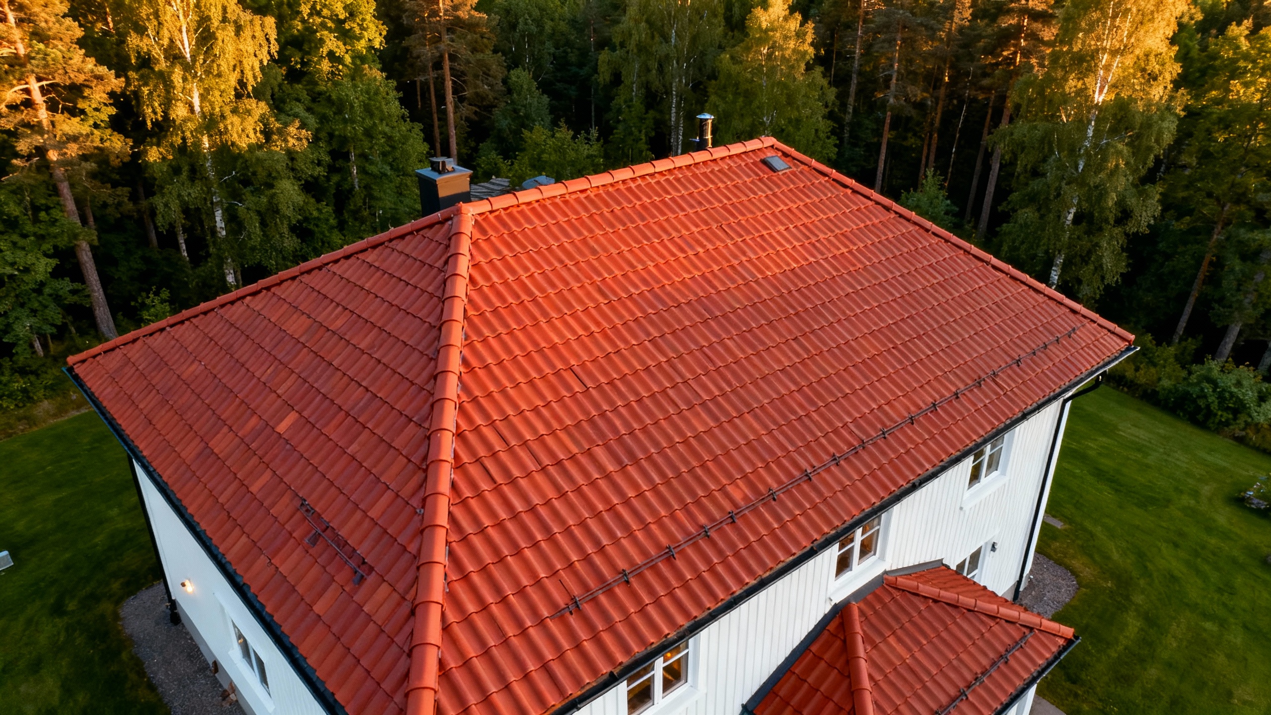 Tegelrött tak på ett vitmålat hus omgivet av grönskande träd.