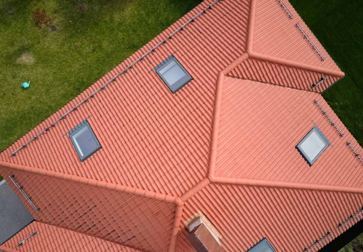 Flygfoto över ett hus med rött tegeltak och flera takfönster, omgivet av grönt gräs.