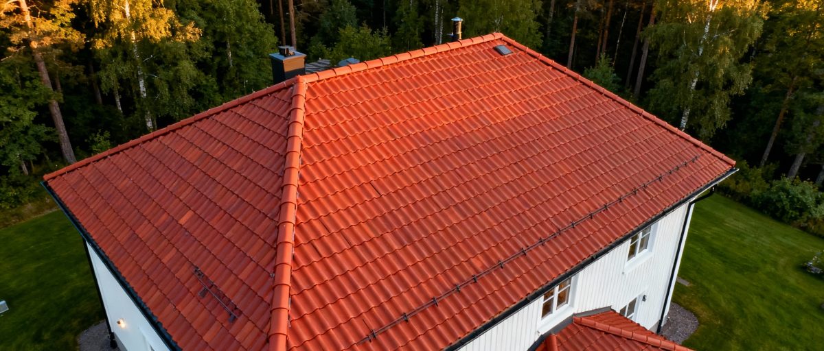 Tegelrött tak på ett vitmålat hus omgivet av grönskande träd.